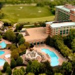 Aerial view of resort property with swimming pools, golf course, and multi-story hotel buildings surrounded by trees