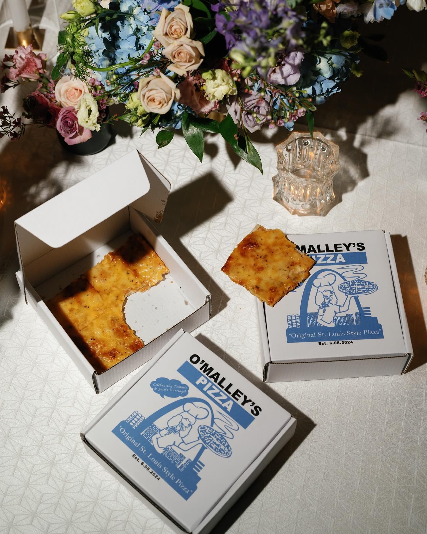 O'Malley's St. Louis style pizza boxes arranged beneath colorful floral centerpiece with crystal glassware