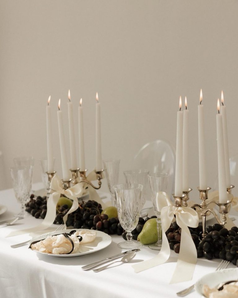 Elegant wedding table setting with brass candelabras, white tapers, crystal glassware, and fresh fruit centerpieces