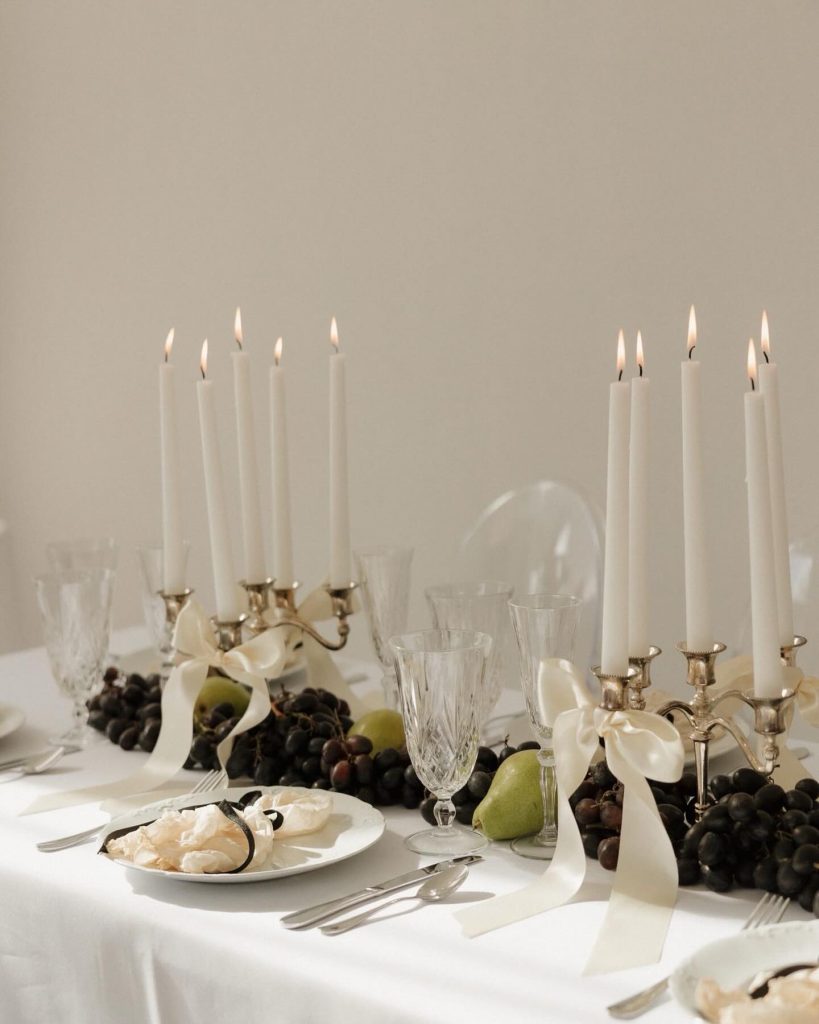 Elegant wedding table setting with brass candelabras, white tapers, crystal glassware, and fresh fruit centerpieces
