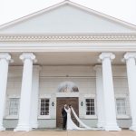Bride and groom embracing under grand white colonial portico with Ionic columns and triangular pediment
