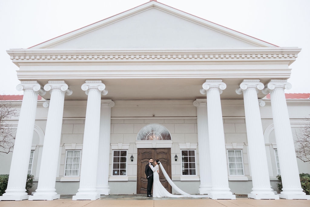 Bride and groom embracing under grand white colonial portico with Ionic columns and triangular pediment