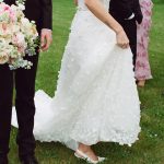 Close-up of bride's textured white gown and groom's black suit as they hold hands on grass