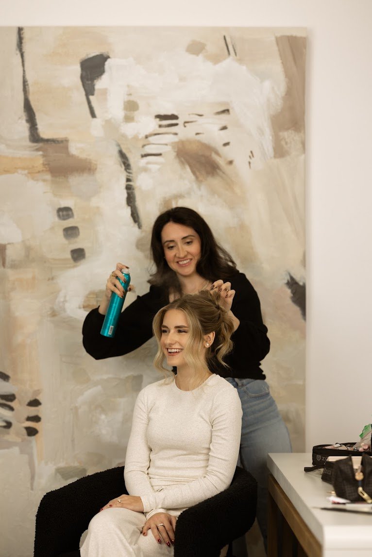 Hairstylist spraying hairspray on bride's textured blonde updo in bright studio