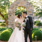 Newlyweds kissing in garden with stone archway and boxwood hedges