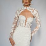 Fitted wedding dress with sheer long sleeves and high neckline featuring white floral lace appliqués