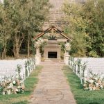 Outdoor ceremony space at The Barn at Ackerhurst Dairy Farm featuring white chairs, floral aisle decor, and stone fireplace