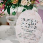 Champagne and nacho caviar bar menu sign with pink floral rose pattern beside colorful wedding centerpiece