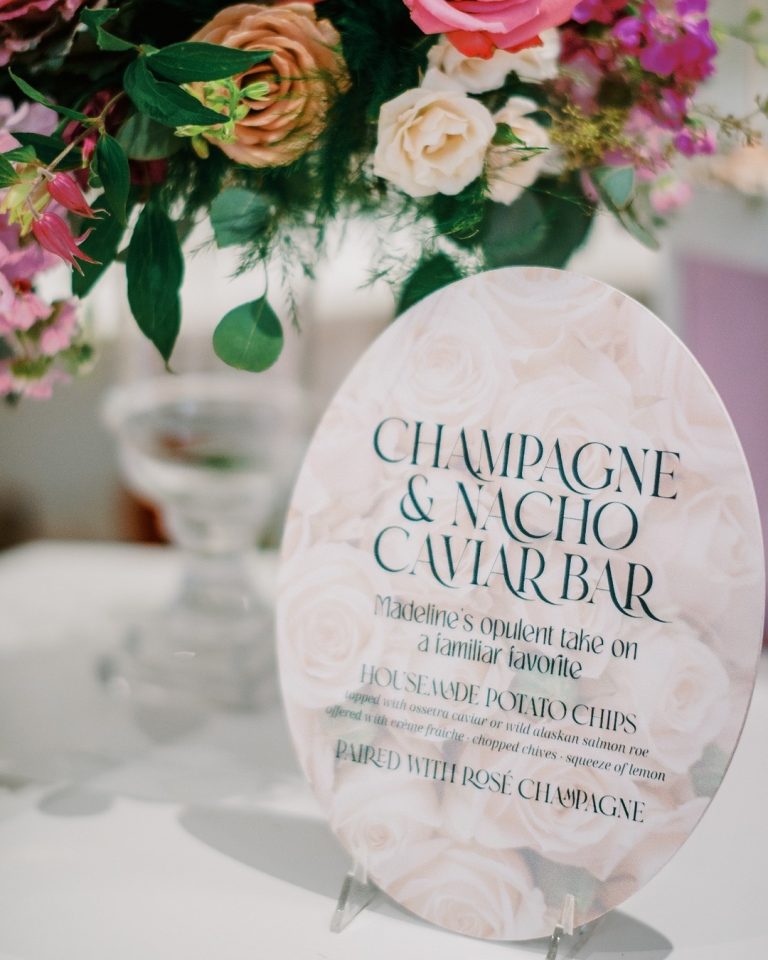 Champagne and nacho caviar bar menu sign with pink floral rose pattern beside colorful wedding centerpiece