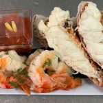 Elegant seafood platter featuring lobster tail, jumbo shrimp with dill, and cocktail sauce with carrot rose garnish