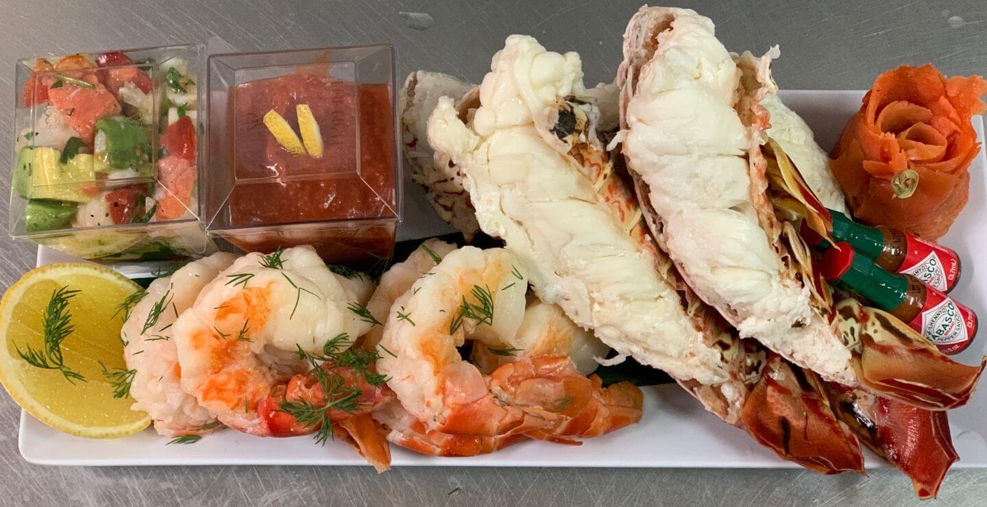 Elegant seafood platter featuring lobster tail, jumbo shrimp with dill, and cocktail sauce with carrot rose garnish