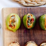 Stuffed avocado halves with vegetables and microgreens on wooden cutting board