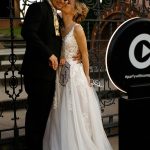 Bride and groom posing with fun props at wedding photo booth near ornate iron gates