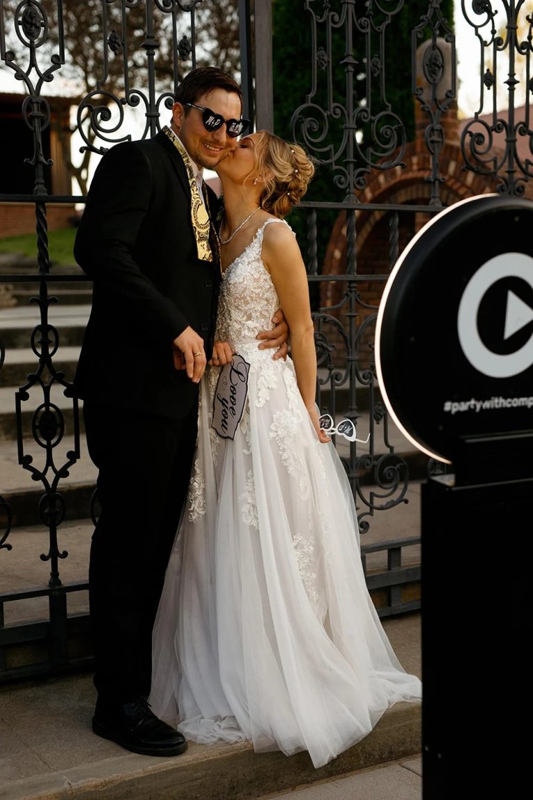 Bride and groom posing with fun props at wedding photo booth near ornate iron gates