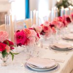 Long formal dining table with pink and red rose centerpieces, taper candles, and elegant place settings