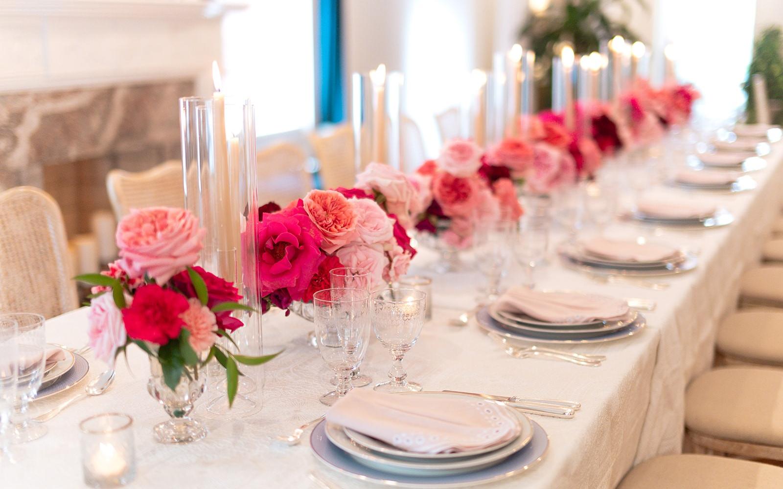 Long formal dining table with pink and red rose centerpieces, taper candles, and elegant place settings