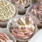 Decorated cupcakes with pink and white frosting, gold lettering, and pearl sprinkles