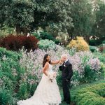 Bride and groom sharing an intimate moment in a lush garden with blooming lavender flowers and colorful shrubs