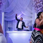 Wedding DJ in tuxedo energizing guests at elegant reception with purple uplighting and floral decor