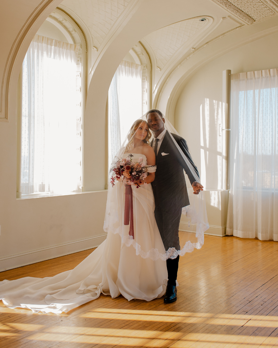 Bride and groom portrait in elegant room with arched windows, vaulted ceiling, and natural sunlight streaming across hardwood floors