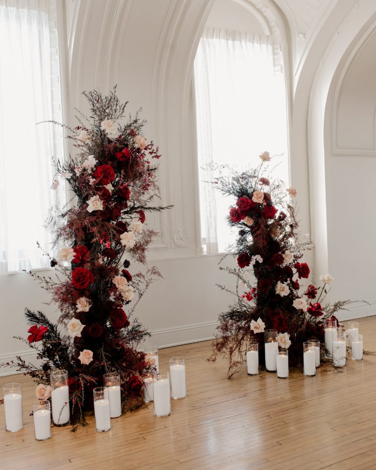 Dramatic floral installations with red and white roses flanking arched windows, surrounded by pillar candles