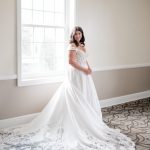 Bride in off-shoulder A-line wedding dress with lace appliqué train in bright room