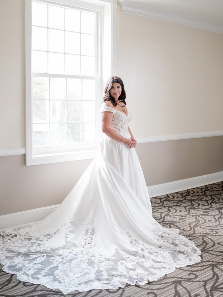 Bride in off-shoulder A-line wedding dress with lace appliqué train in bright room