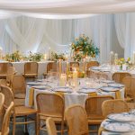 Overview of elegant wedding reception venue with round tables, draped ceiling, and orange and white floral decor