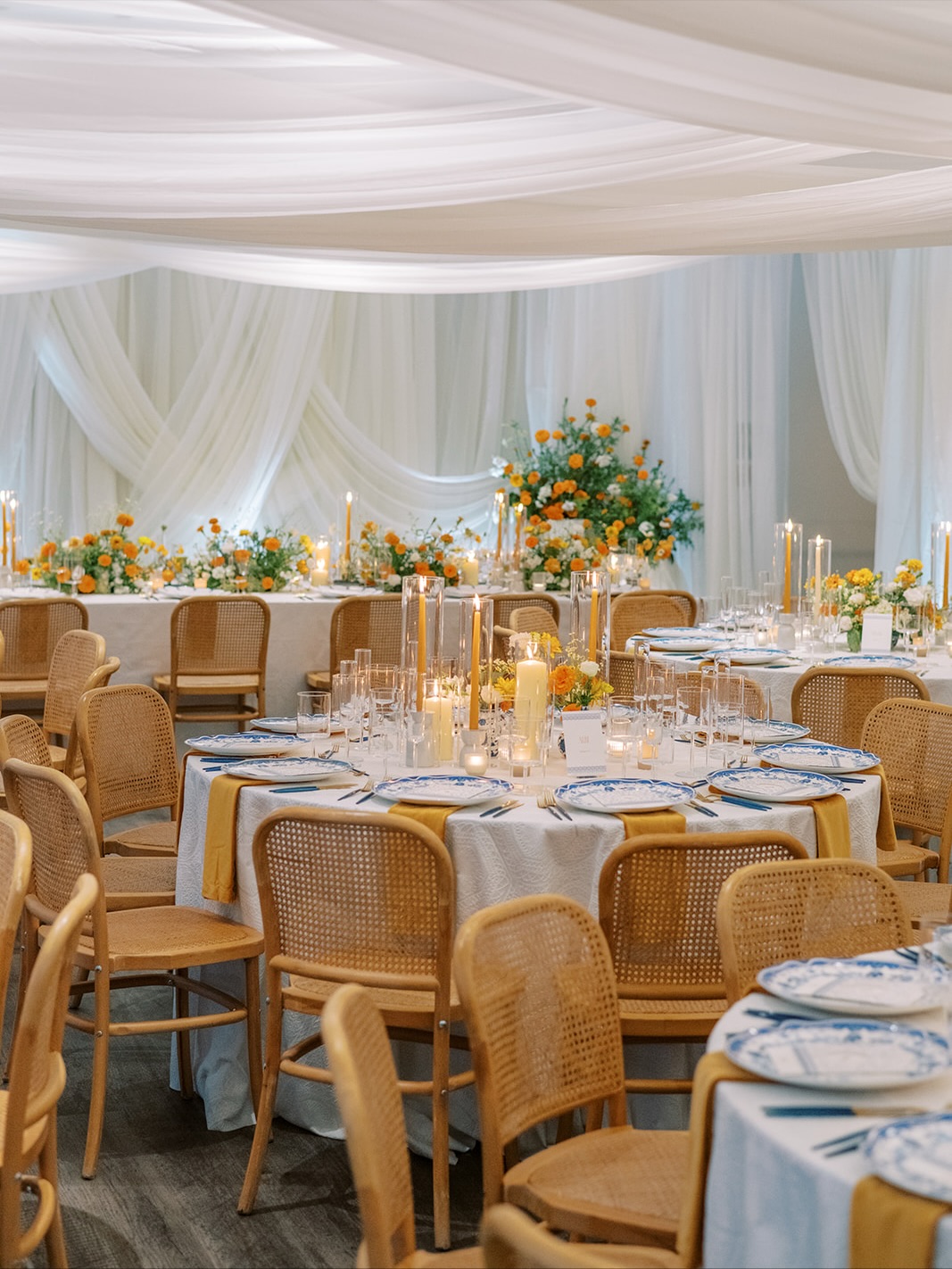 Overview of elegant wedding reception venue with round tables, draped ceiling, and orange and white floral decor