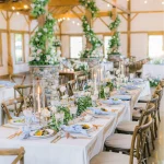 Rustic barn wedding reception tables with greenery garlands, tall candles, and blue napkins