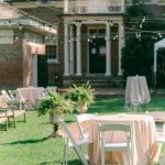 Garden reception area with bistro tables, string lighting, and historic columned mansion in background