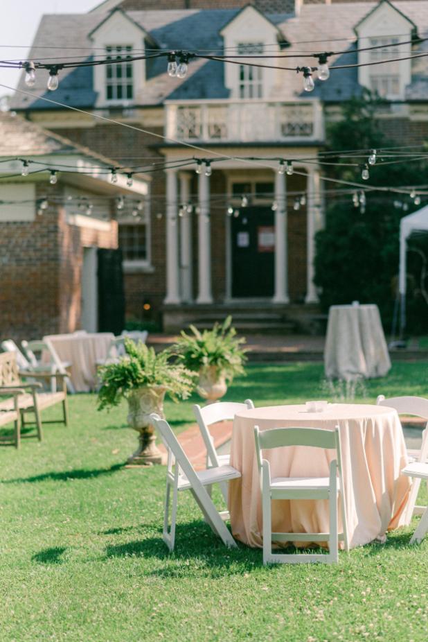 Garden reception area with bistro tables, string lighting, and historic columned mansion in background