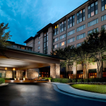 Upscale hotel entrance at twilight featuring stone columns, covered porte-cochere, and landscaped circular driveway