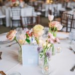 Wedding reception table with pastel floral centerpieces in small vases, candles, and string lights in rustic barn venue