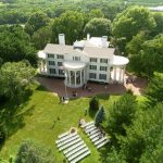 Aerial view of white columned mansion wedding venue with ceremony seating on manicured lawn surrounded by trees