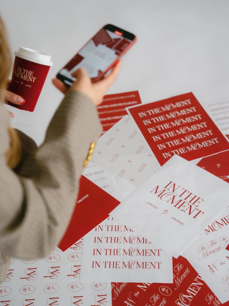 Content creator photographing branded marketing materials with coffee cup and smartphone