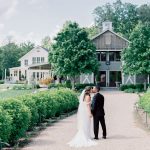 Bride and groom kissing on gravel path at rustic Northern Virginia farm wedding venue with barn buildings