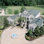 Aerial view of luxury estate wedding venue with white stucco buildings, central fountain, and vineyard landscape