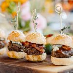 Gourmet mini burger sliders with bacon and cheese on wooden board, garnished with fresh herbs