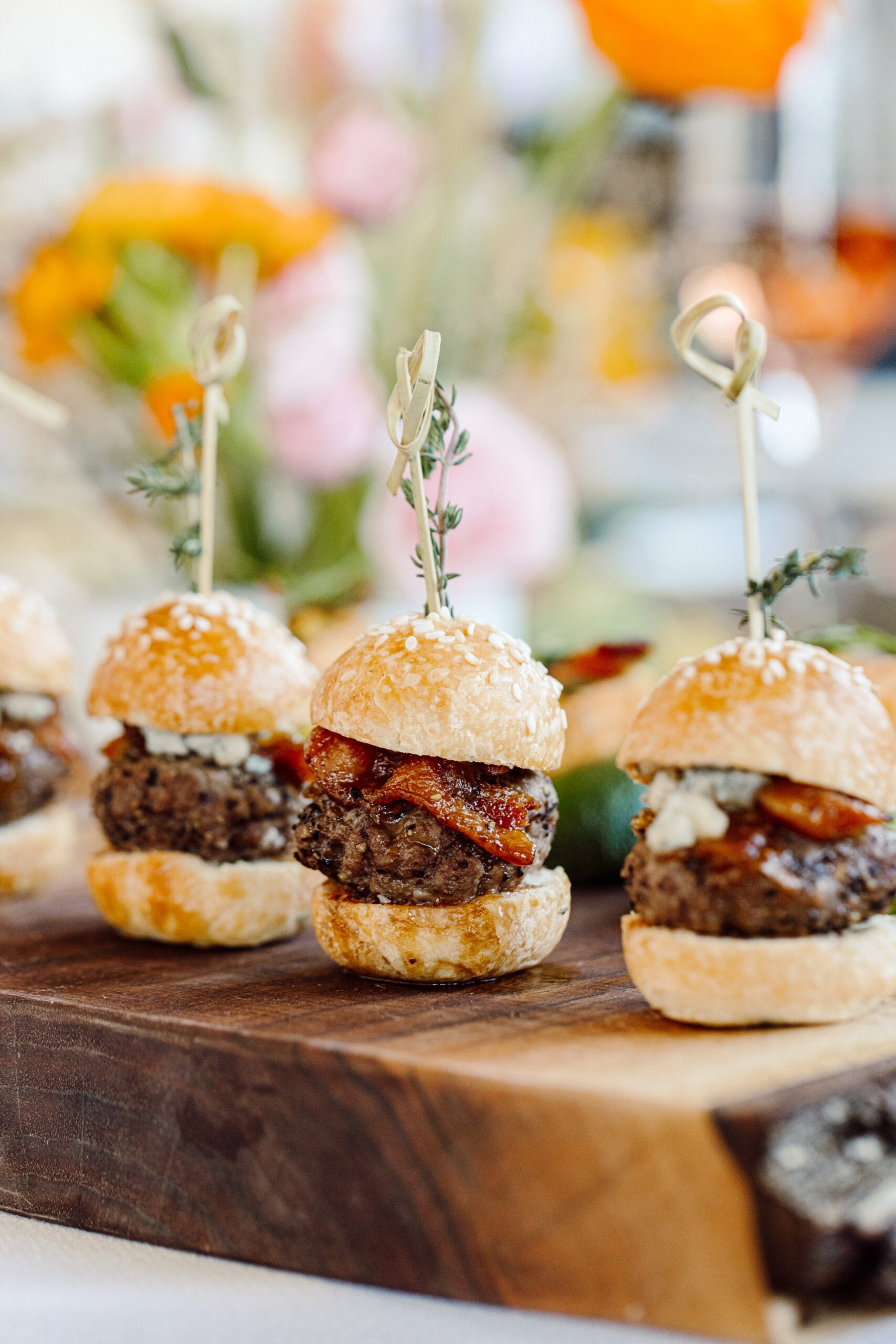 Gourmet mini burger sliders with bacon and cheese on wooden board, garnished with fresh herbs