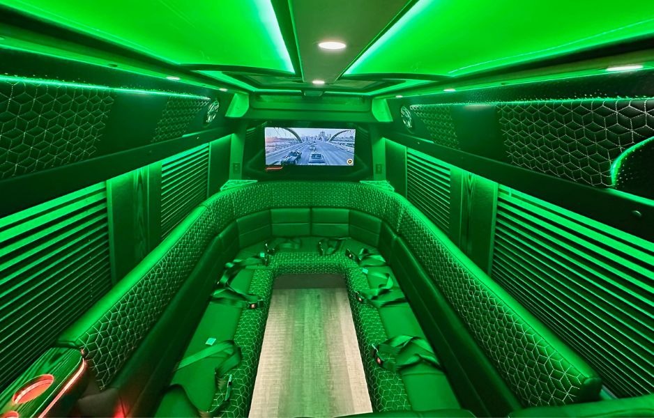 Spacious party bus interior featuring green LED lighting, quilted leather bench seating, and flat-screen TV