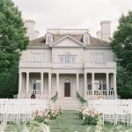 White neoclassical mansion with columned portico and outdoor wedding ceremony setup with white chairs on manicured lawn