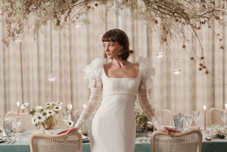 Bride in modern wedding dress with dramatic ruffled shoulders and sheer sleeves at elegant candlelit reception