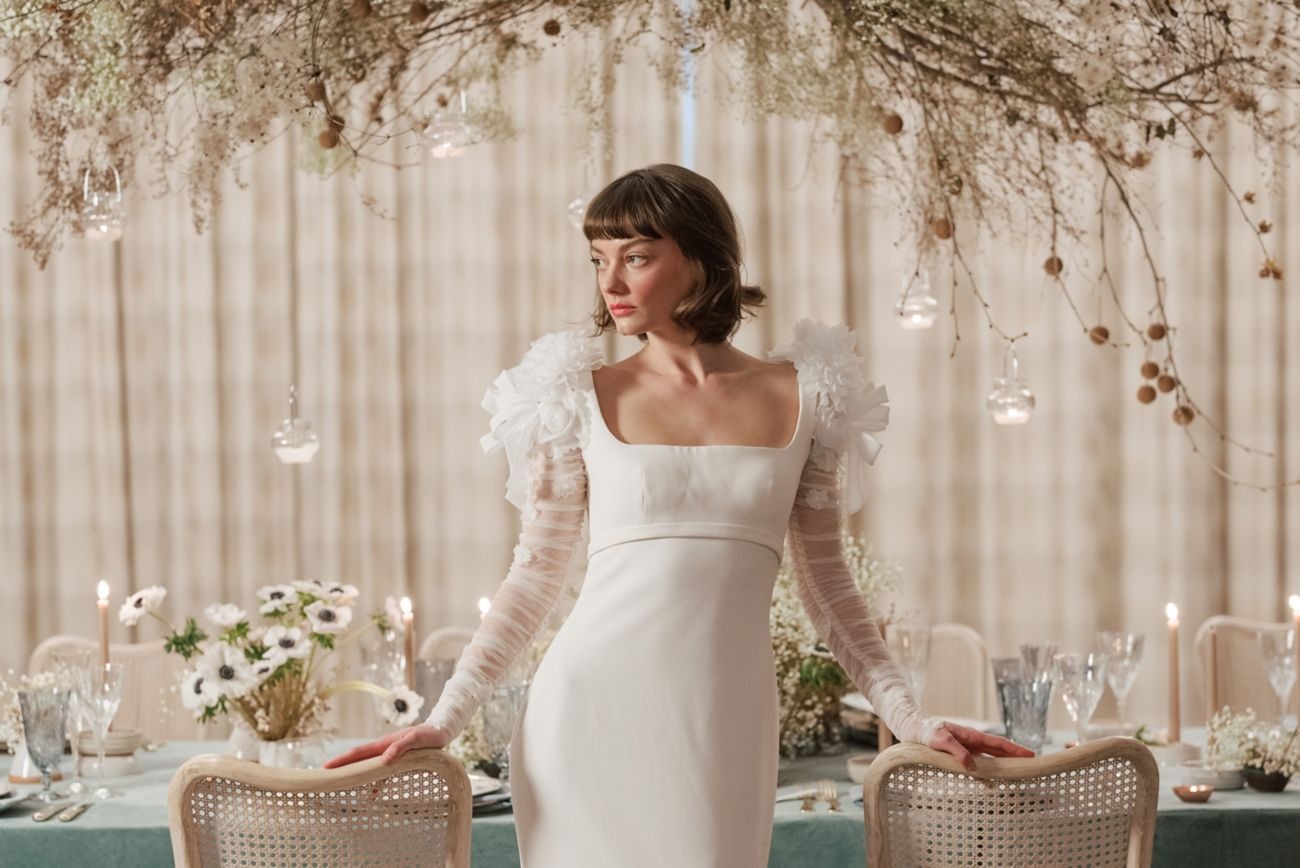 Bride in modern wedding dress with dramatic ruffled shoulders and sheer sleeves at elegant candlelit reception