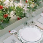 Place setting with decorative circular name card featuring coral swirl design, green-trimmed plates, and silver flatware