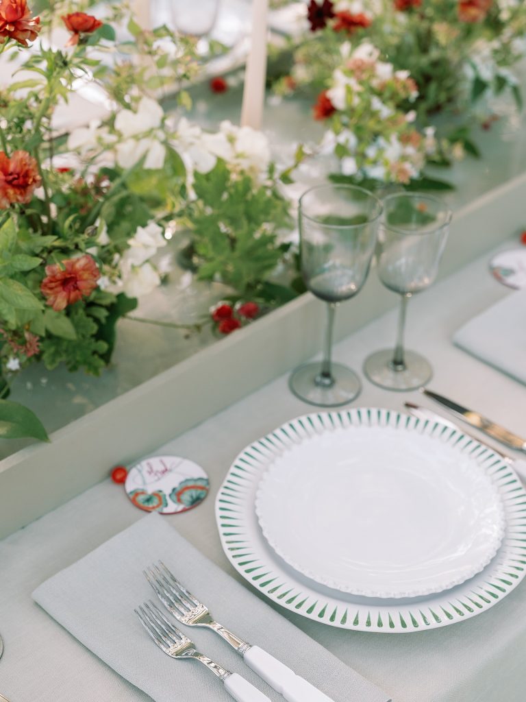 Place setting with decorative circular name card featuring coral swirl design, green-trimmed plates, and silver flatware