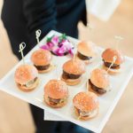 Server holding tray of mini burger sliders garnished with sesame seeds at Northern Virginia catered event