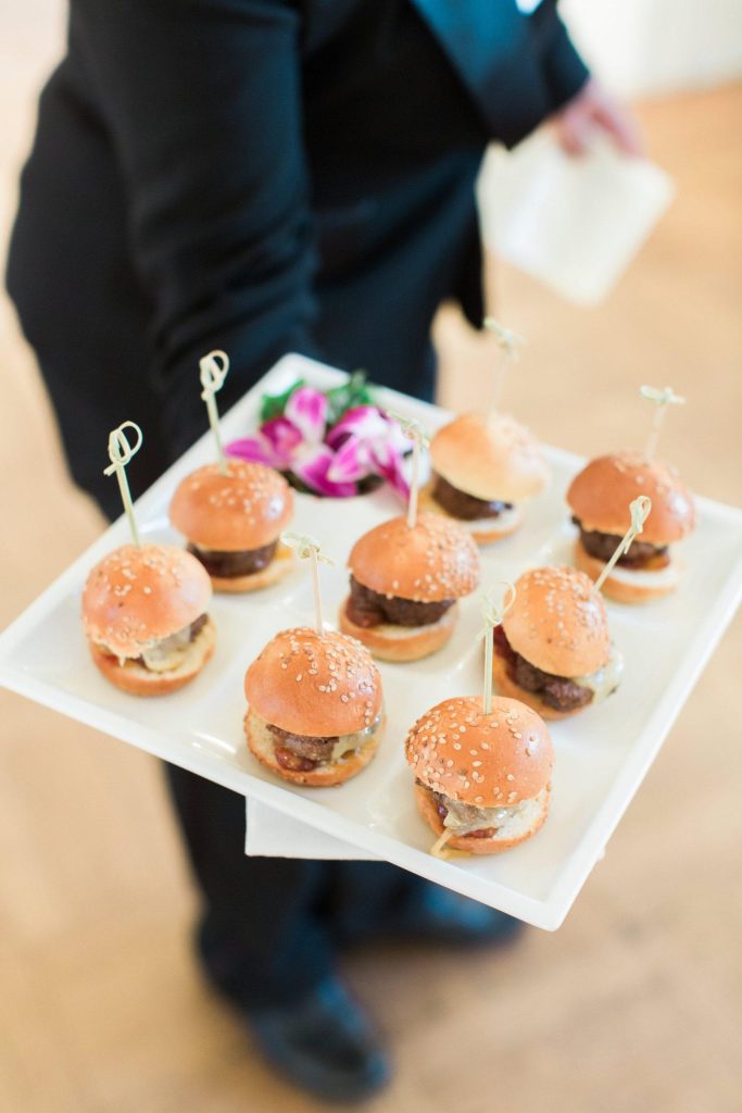 Server holding tray of mini burger sliders garnished with sesame seeds at Northern Virginia catered event