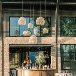 Outdoor bar setup with woven pendant lights, wooden bar, and patterned cocktail table linens