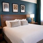 Hotel room with teal accent wall, wooden headboard, white bedding, and architectural artwork
